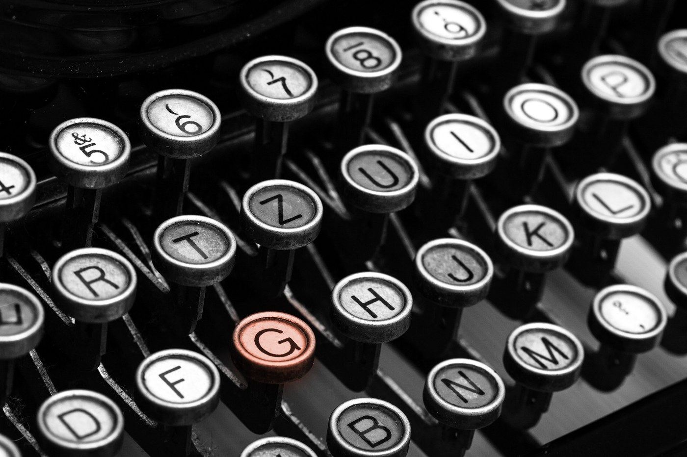 Close-up of vintage typewriter keys in black and white, with the G key picked out in salmon